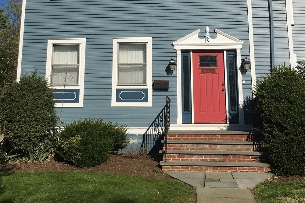 close up of first floor of blue house with white trim and red door